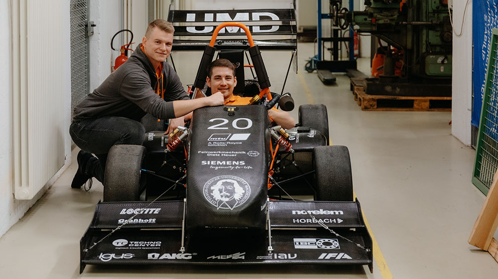 Daniel Senst (links) und Martin Roye (rechts) mit dem Elektrorennwagen von UMD Racing (Foto: Hannah Theile / Uni Magdeburg)