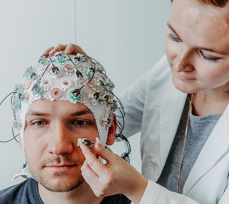 Die technische Assistentin Christina Becker legt dem Probanden eine Kappe mit Elektroden zur Messung der Hirnströme (EEG) an. Foto: CBBS, OVGU Magdeburg, D. Mahler