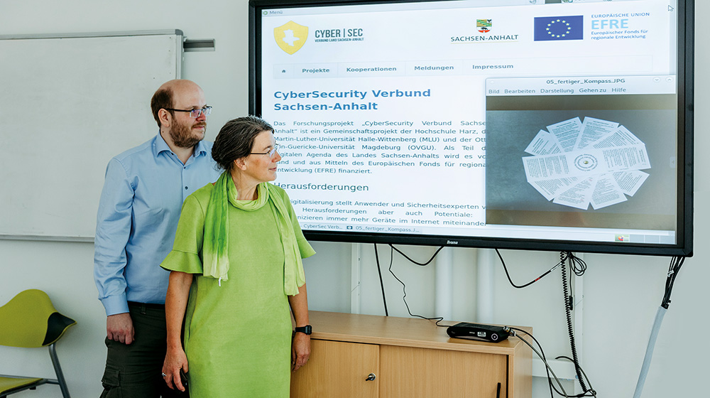 Robert Altschaffel und Jana Dittmann stehen vor einem großen Bildschirm, auf dem ihr Kompass zur digitalen Selbstverteidigung zu sehen ist (c) Jana Dünnhaupt Uni Magdeburg