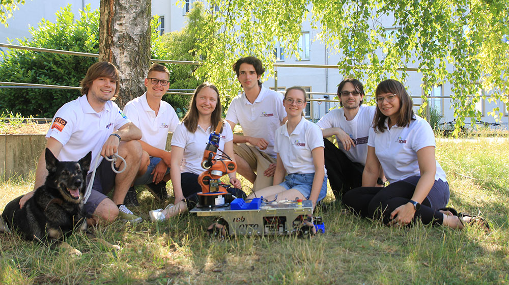 Das Team von Robotto mit Hund und ihrem Roboter auf einer Wiese des Unicampus (c) privat