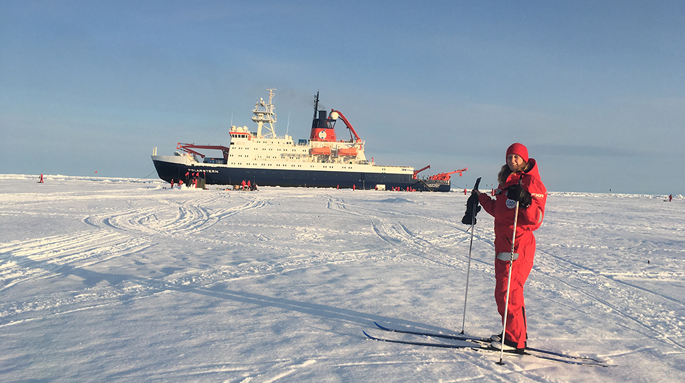 Dr. Carolin Mehlmann stands with skis on the ice at the North Pole in front of the research vessel Polarstern (c) Thomas Richter / Carolin Mehlmann