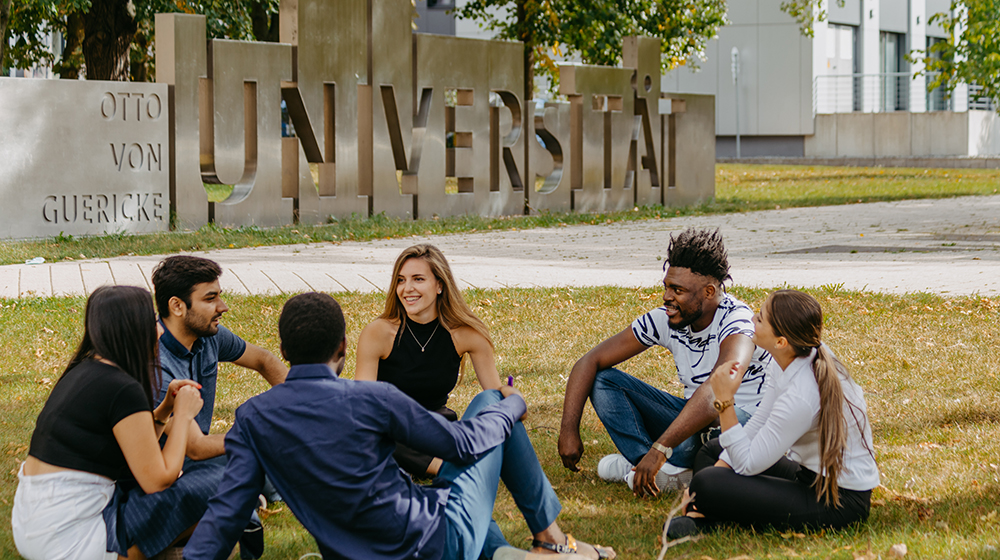 Internationale Studierende sitzen auf der Wiese vor der Uniporta (Foto: Hannah Theile / Uni Magdeburg)