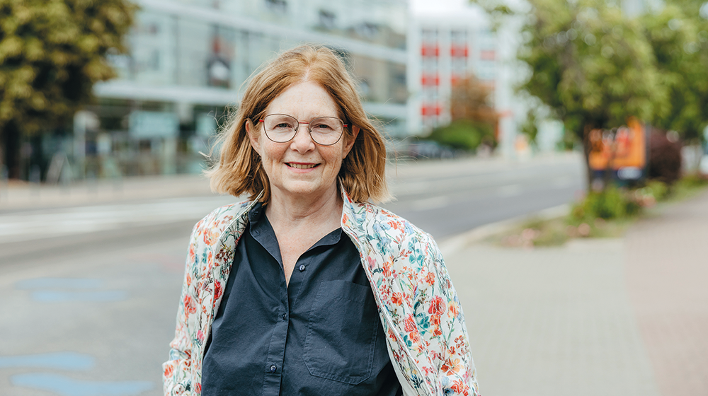 Portrait Prof. Ellen Matthies auf einem Gehweg vor dem Campus mit einem Gebäude und Bäumen im Hintergrund (c) Jana Dünnhaupt Uni Magdeburg