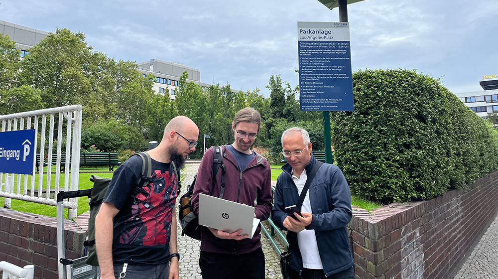 Marian Buschsieweke, Frank Engelhardt und Mesut Günes schauen auf einen Laptop, hinter ihnen das Zeichen einer Parkgarage (c) privat
