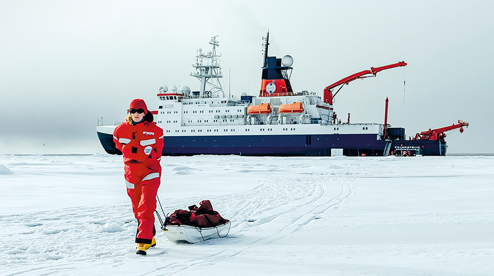 Carolin Mehlmann pulls material across the floe, in the background the Polarstern (Photo: Thomas Richter)