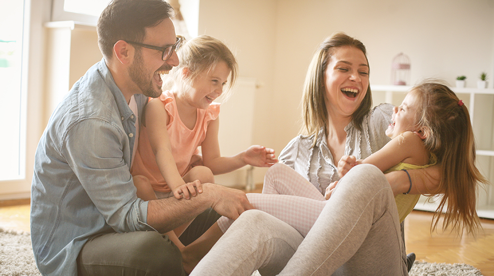 Fröhliche Familie mit zwei Töchtern, die zu Hause spielen. Familie sitzt auf dem Boden und spielt zusammen.