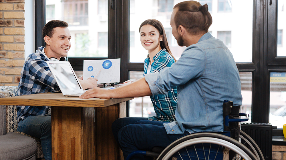 Studierende sitzen an einem Tisch und unterhalten sich - ein Student sitzt im Rollstuhl (Foto: Shutterstock / YAKOBCHUK VIACHESLAV)