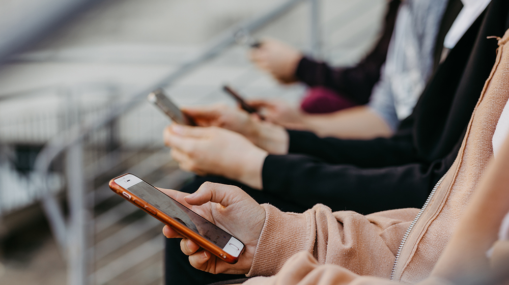 Studierende sitzen auf einer Treppe und schauen auf ihr Smartphone (Foto: Jana Dünnhaupt / Uni Magdeburg)