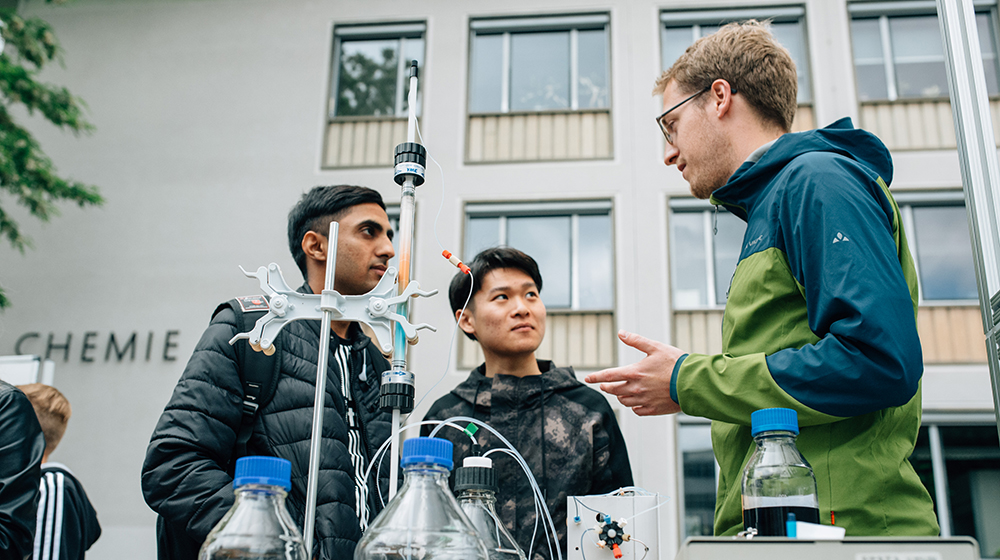 /unimagdeburg_media/Presse/Bilder/Pressemitteilungen/2023/2+junge+M%C3%A4nner+im+Gespr%C3%A4ch+mit+einem+Wissenschaftler+auf+dem+Campus_+im+Vordergrund+des+Bildes+Reagenzgl%C3%A4ser+und+ein+Versuchsaufbau+%28c%29+Matthias+Sasse-height-560-width-1000-p-107416.jpg