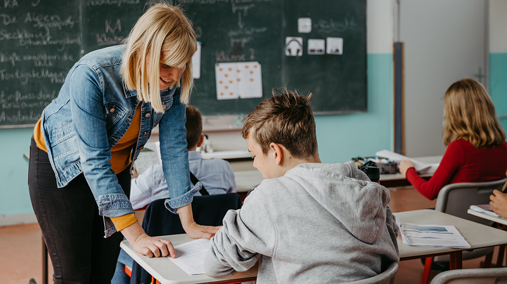 /unimagdeburg_media/Presse/Bilder/Pressemitteilungen/2023/Eine+Lehrerin+im+Gespr%C3%A4ch+mit+einem+m%C3%A4nnlichen+Sch%C3%BCler_+hinter+ihnen+eine+Tafel+mit+Text_+zwei+Sch%C3%BClerInnen+arbeiten+an+Aufgaben+%28c%29+Jana+D%C3%BCnnhaupt+Uni+Magdeburg-height-560-width-1000-p-107436.jpg