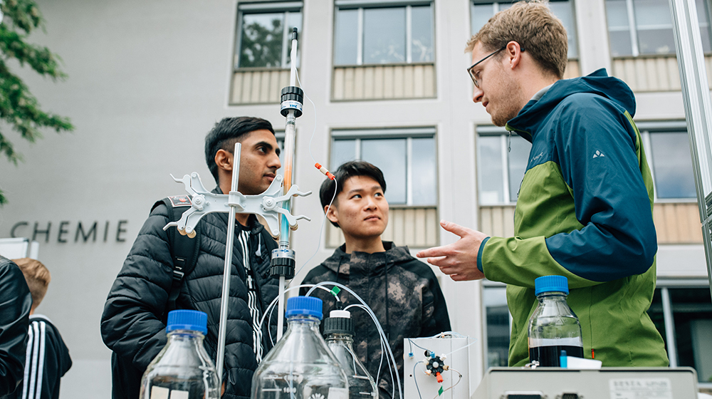 /unimagdeburg_media/Presse/Bilder/Pressemitteilungen/2023/Zwei+junge+M%C3%A4nner+im+Gespr%C3%A4ch+mit+einem+Wissenschaftler+auf+dem+Campus_+im+Vordergrund+des+Bildes+Reagenzgl%C3%A4ser+und+ein+Versuchsaufbau+%28c%29+Matthias+Sasse-height-560-width-1000-p-106354.jpg