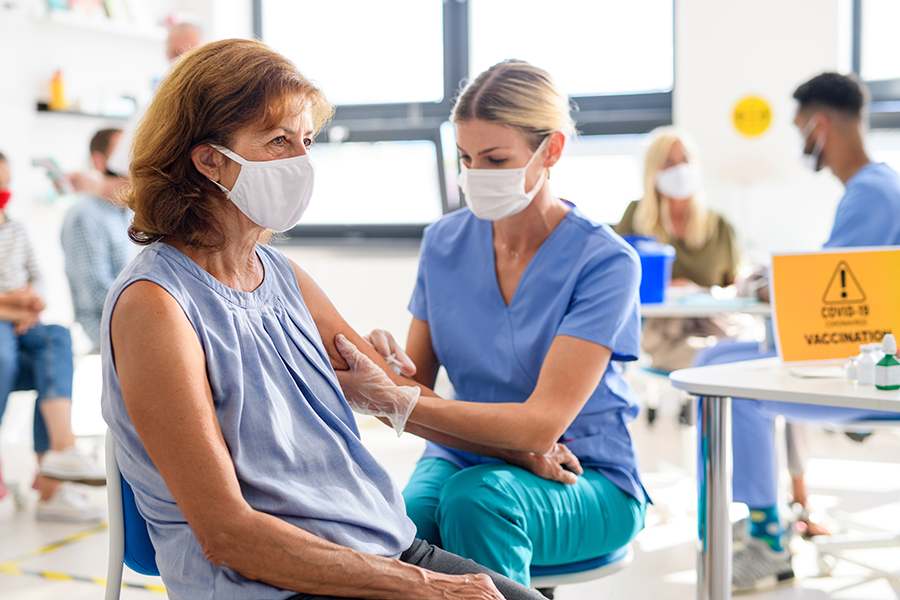 Frau mit Gesichtsmaske wird geimpft (c) Shutterstock Halfpoint